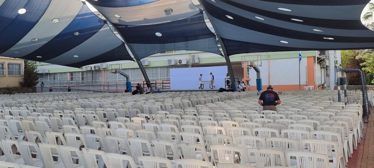 שטח אירועים פתוח עם שורות כיסאות רבות וקירוי הצללה גדול, מוכן לאירוע חברה.
